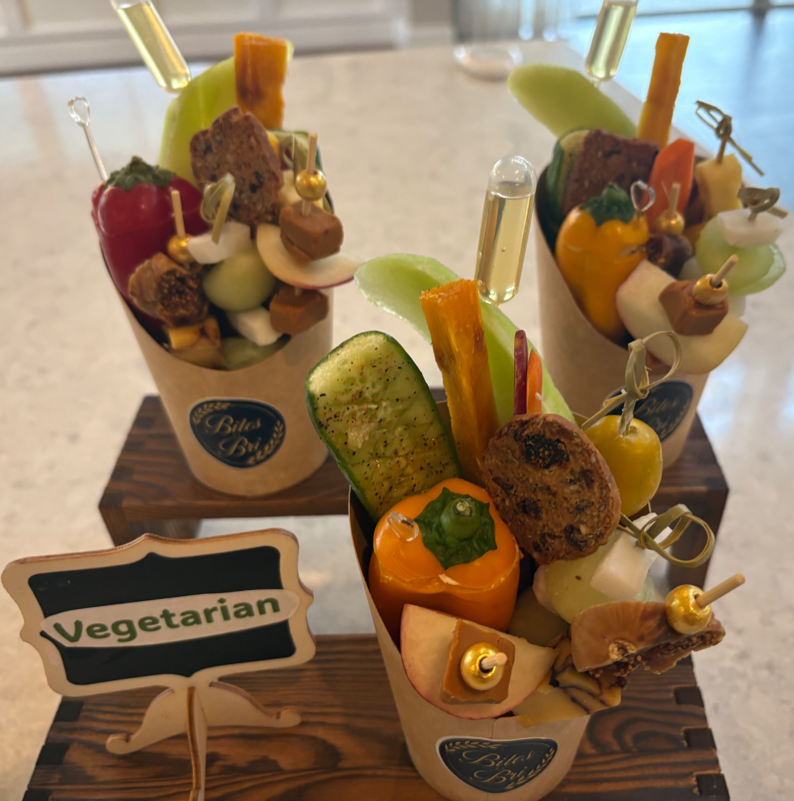 Three Bites by Bri vegetarian cups displayed on wooden stands.